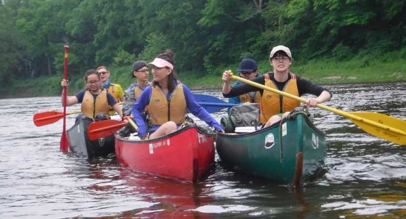 A group of people wearing lifejackets paddle canoes 